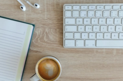 Notebook and keyboard on a desk next to a cup of coffee